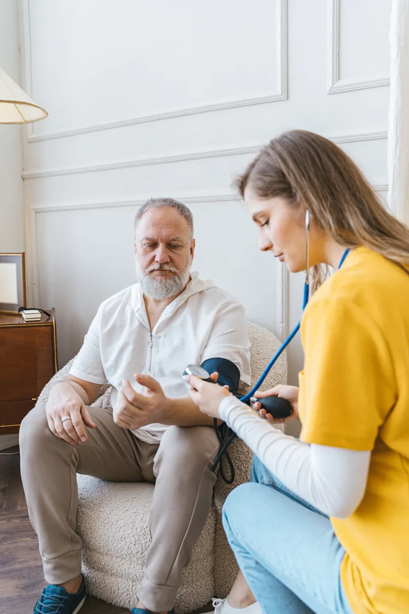 A registered nurse checking an older man's blood pressure at home