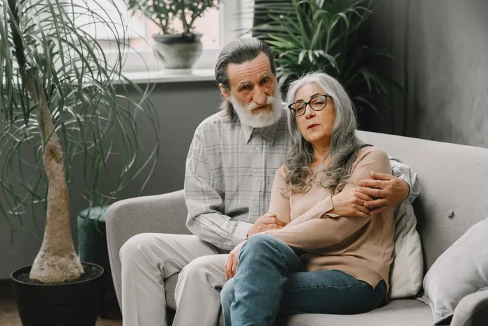 An older couple sitting close together on the sofa of their own home